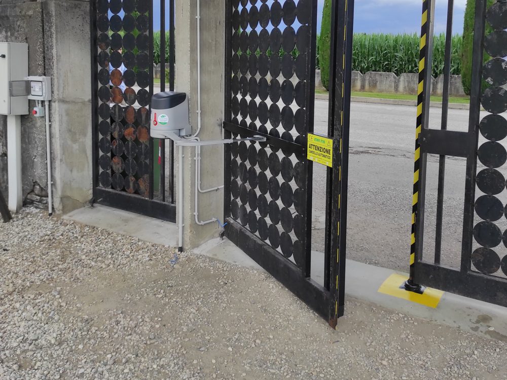 Motoriduttore Nice installato su un cancello a battente, con canalina, fotocellula e cartello di avvertimento