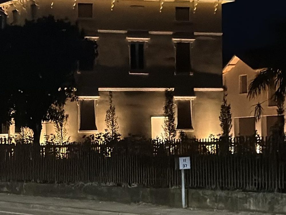 Facciata di una villa illuminata dal basso di notte, con le alberature in controluce