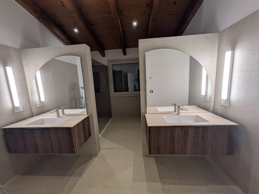 Bagno con doppio lavabo, faretti a soffitto e applique verticali accanto agli specchi